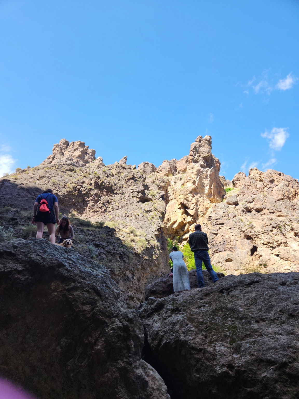 Visitors climbing a rugged rocky canyon beneath a wide blue sky.