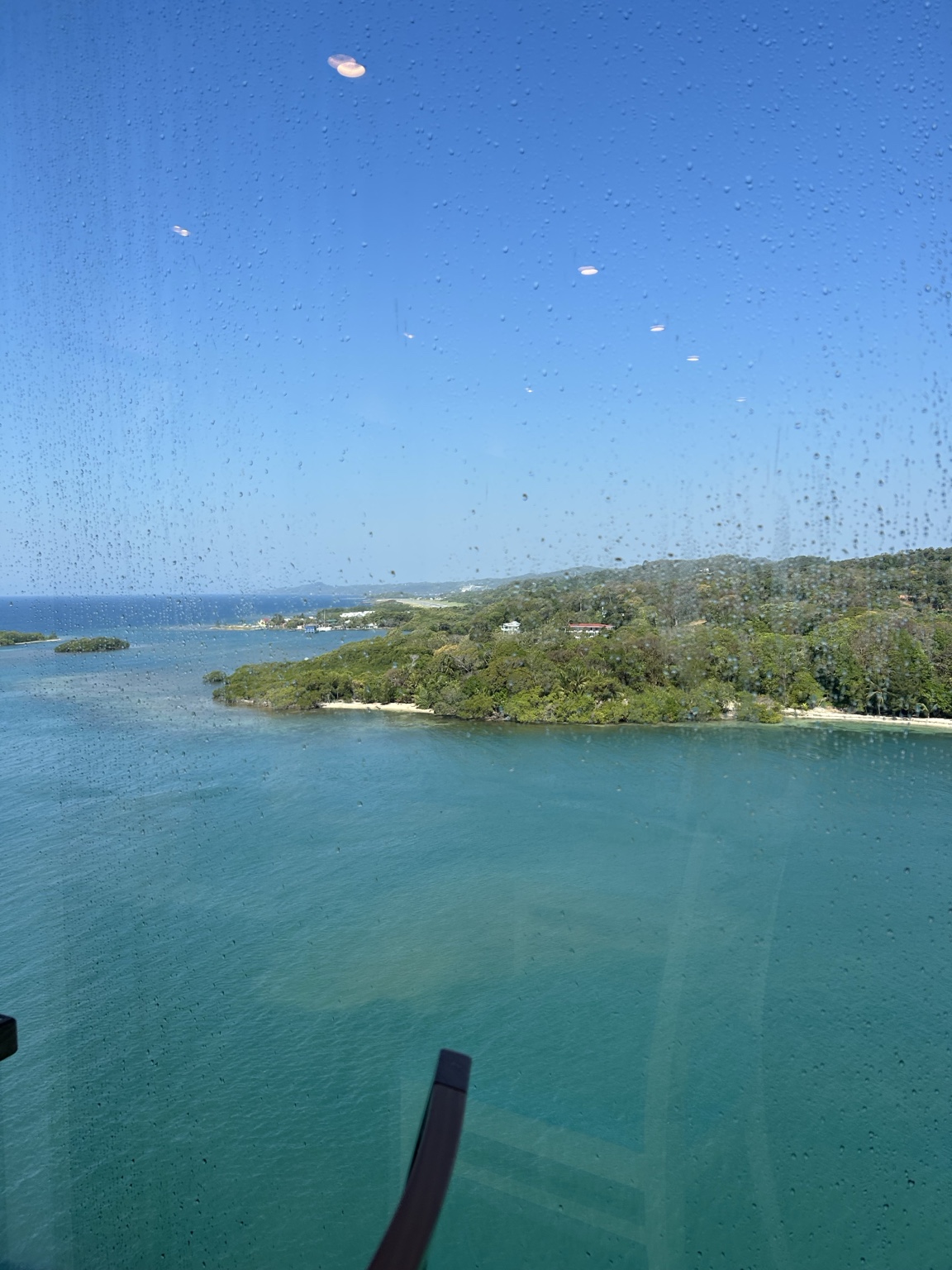 Blue-green water, green shoreline, and distant islands seen through a rain-speckled window.