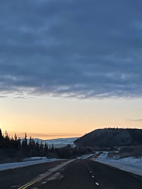 A quiet road crosses a snowy landscape beneath a blue-gray evening sky.