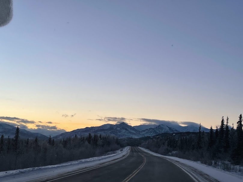 A snow-lined road leads toward distant mountains at dusk.